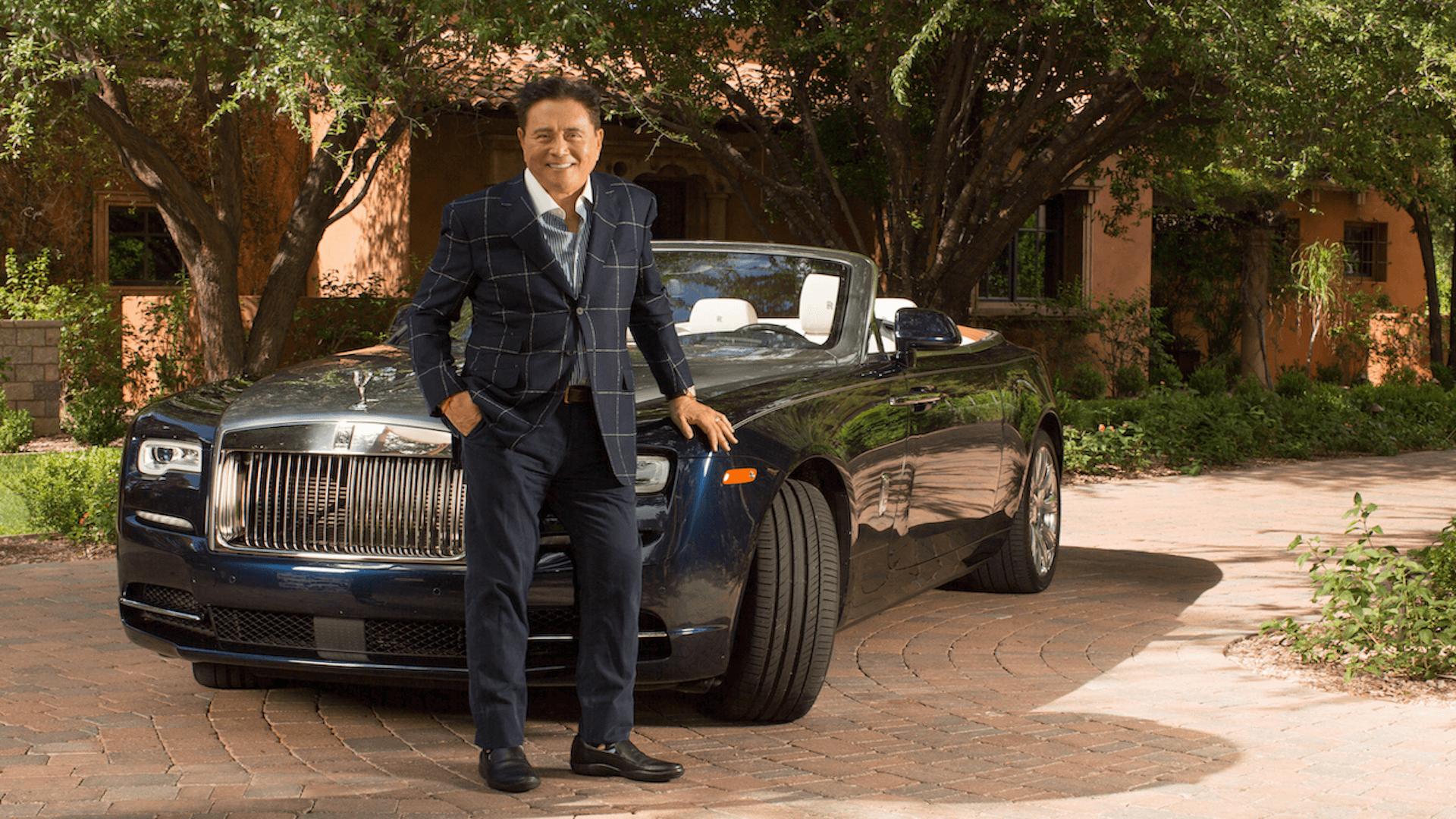 Robert Kiyosaki ao lado de um Rolls-Royce, simbolizando sucesso financeiro e a estratégia de usar dívidas para gerar riqueza ensinada em Pai Rico Pai Pobre